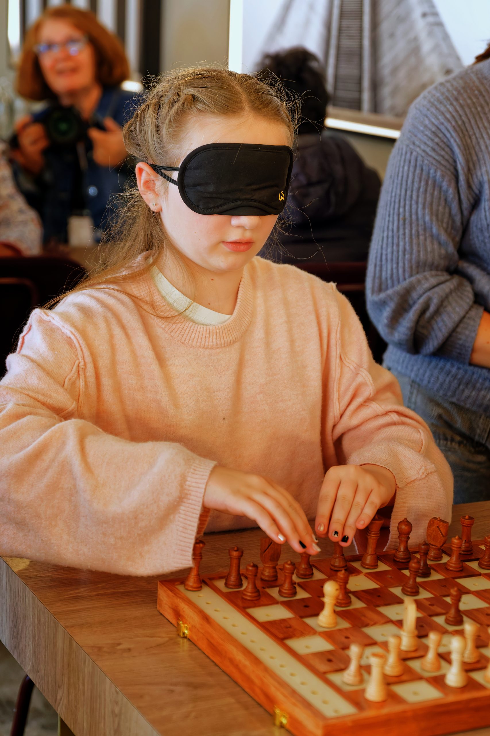 Une jeune fille avec les yeux bandés joue une partie d'échecs sur un échiquier à trous. Elle touche les pièces pour tenter de les distinguer.