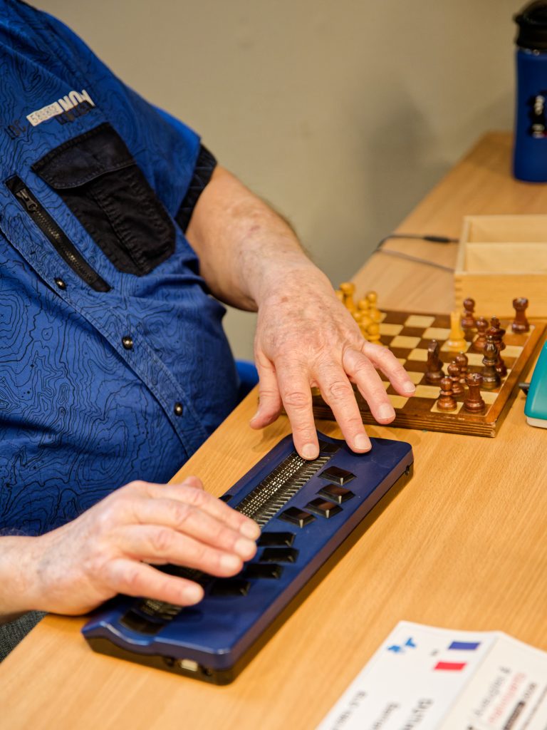 Les mains de Bernard DUTHOIT sur son clavier braille électronique bleu foncé.