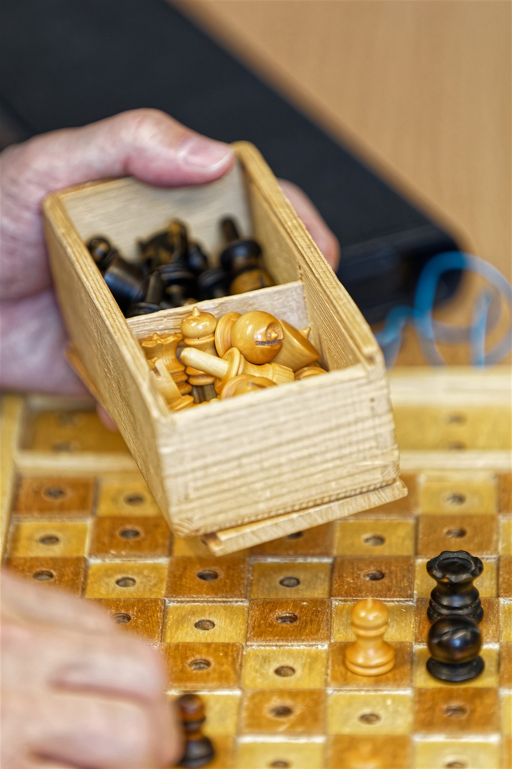 Gros plan sur un jeu d'échecs enfichable en train d'être rangé dans une petite boîte en bois. Il s'agit d'un jeu québécois, car les picots sont sur les pièces blanches au lieu des pièces noires.