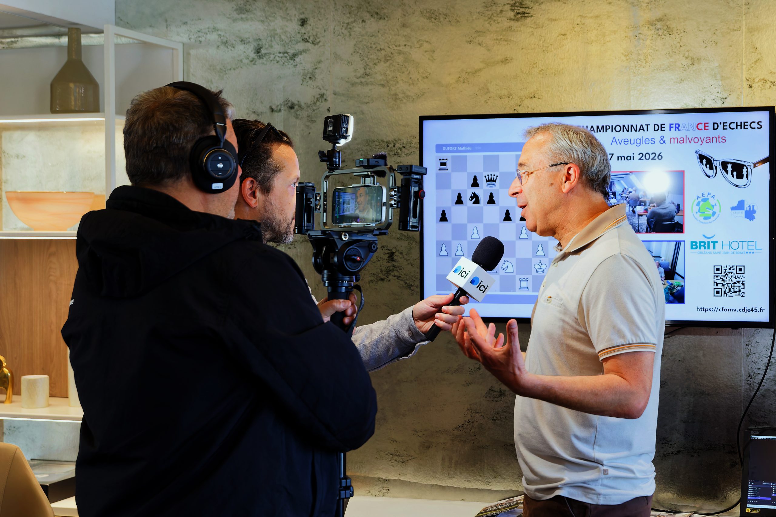 Stéphane, animateur pour le CDJE et bénévole pendant le tournoi, se fait interviewer par une équipe de France 3 devant l'écran de retransmission.