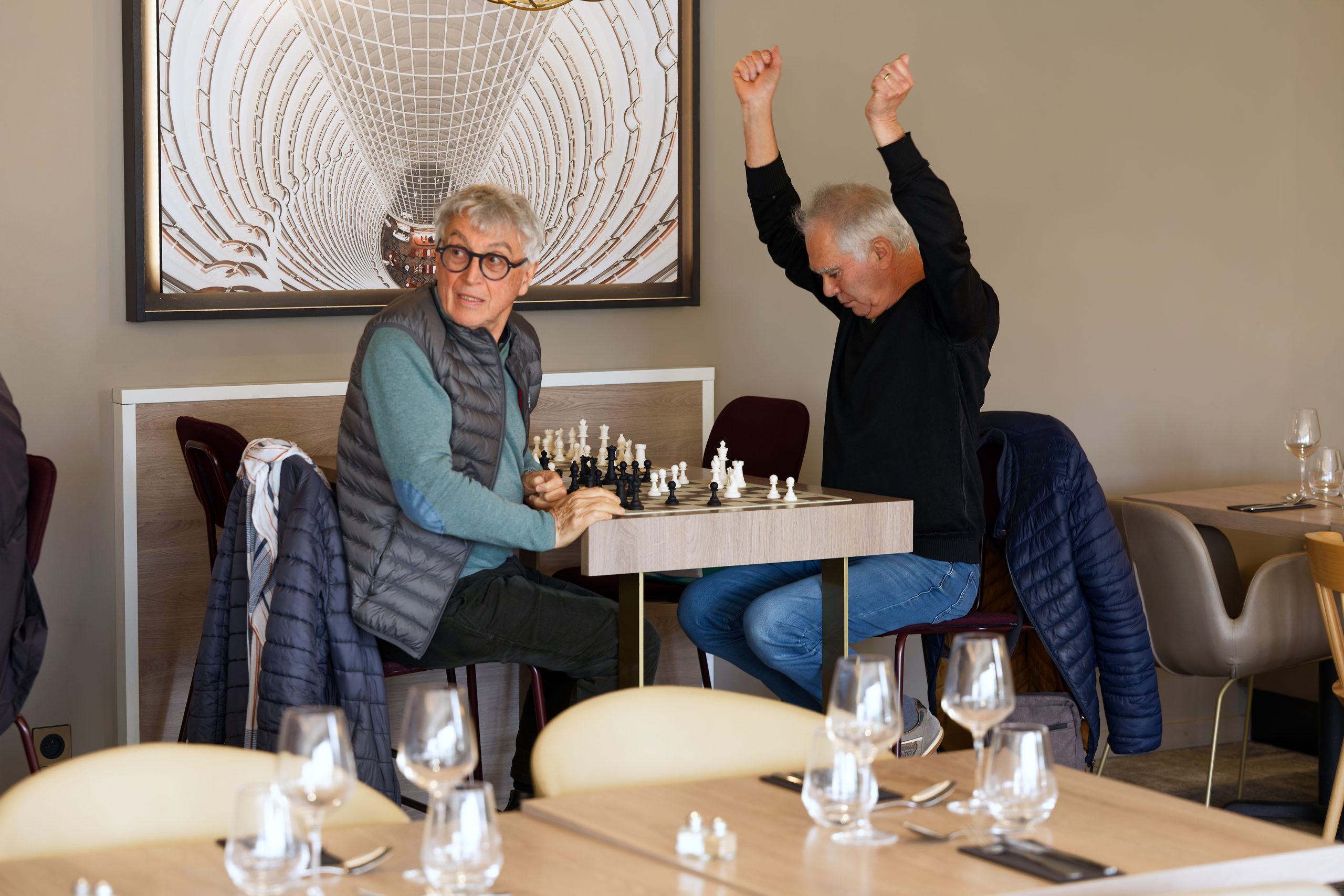 Pendant que les parties se déroulaient, des joueurs d'échecs du département ont pu venir jouer quelques parties dans la salle de restauration. Ici, Jean-Claude lève les bras au ciel, comme s'il venait de remporter la victoire et que sa vie en dépendait, pendant que son adversaire a le dos tourné.