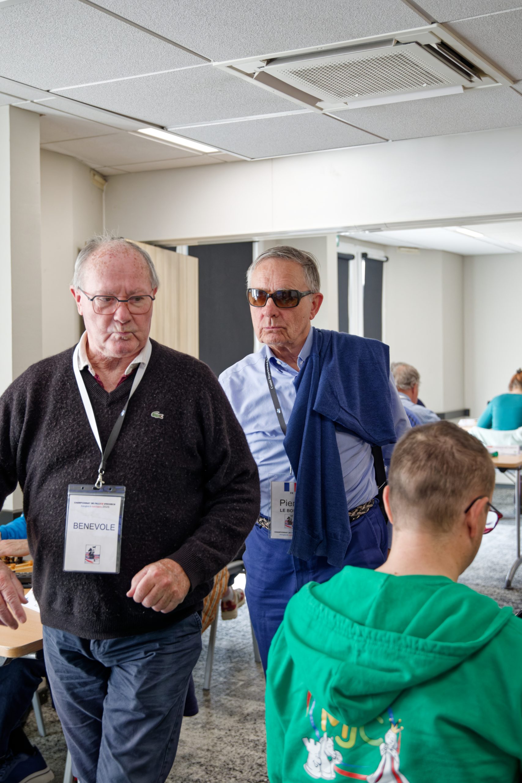 Un membre du Lions club, arborant un badge "Bénévole" escorte Pierre LE BOUILL hors de la salle.